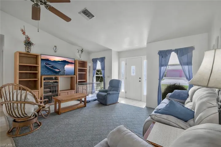 Living room featuring lofted ceiling, ceiling fan, visible vents, and carpet flooring
