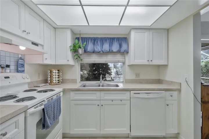 Kitchen featuring white appliances, light countertops, a sink, and white cabinets