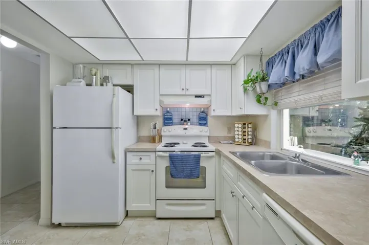 Kitchen featuring white appliances, under cabinet range hood, white cabinetry, and a sink
