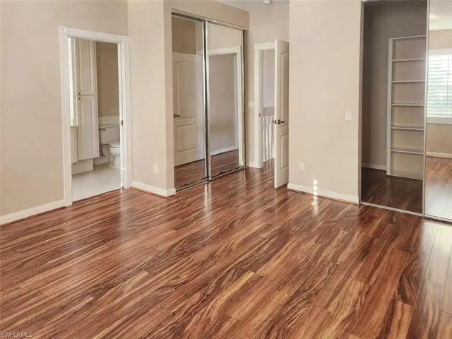 Unfurnished bedroom with connected bathroom, a closet, baseboards, and wood finished floors