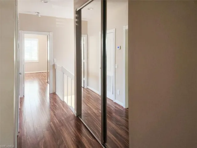 Hallway featuring dark wood-style floors, visible vents, and an upstairs landing