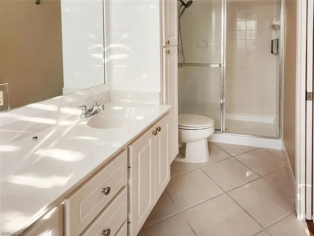 Full bathroom featuring double vanity, a stall shower, toilet, tile patterned flooring, and a sink