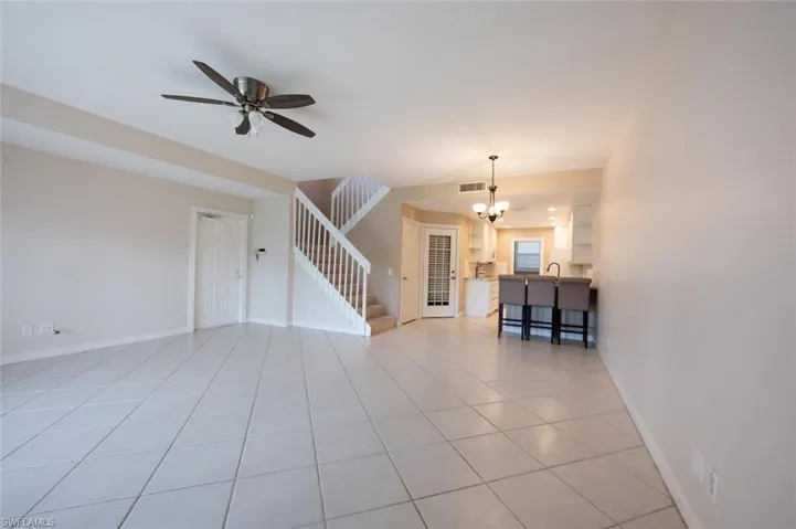 Spare room with light tile patterned floors, baseboards, visible vents, stairs, and ceiling fan with notable chandelier