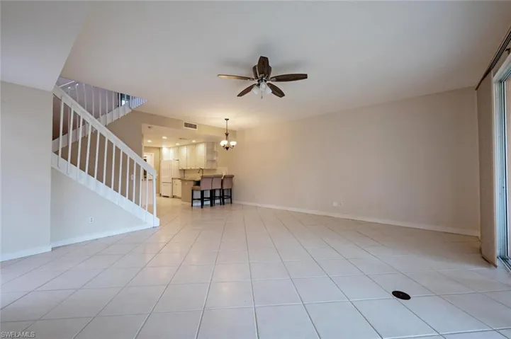 Unfurnished living room with light tile patterned floors, ceiling fan with notable chandelier, visible vents, baseboards, and stairs