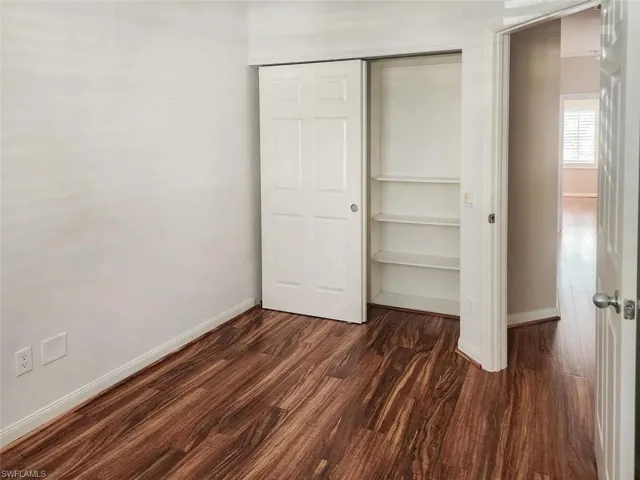 Unfurnished bedroom featuring a closet, dark wood-style flooring, and baseboards