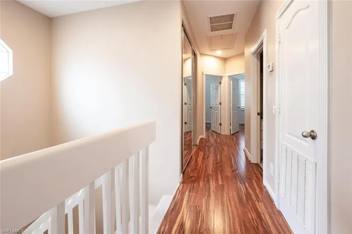 Hall with baseboards, visible vents, and wood finished floors