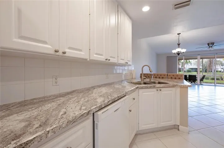 Kitchen with white dishwasher, light tile patterned flooring, a sink, white cabinetry, and decorative backsplash