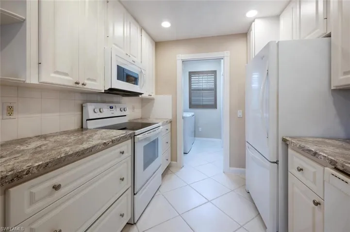 Kitchen featuring light stone counters, tasteful backsplash, white cabinetry, white appliances, and baseboards