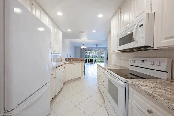 Kitchen with white appliances, light tile patterned floors, a peninsula, a sink, and backsplash