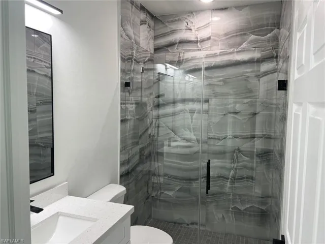Bathroom with a shower with shower door, vanity, and toilet