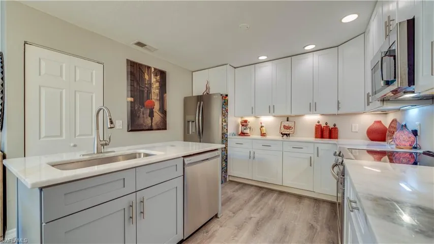 Kitchen featuring white cabinetry, wood-finish flooring, a central island with a sink, stainless steel appliances, and recessed lighting