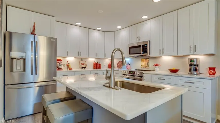 Kitchen featuring white shaker-style cabinetry, stone countertops, stainless steel appliances, a central island with an integrated sink, and recessed lighting
