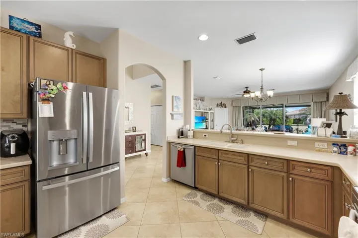 Kitchen featuring brown cabinets, appliances with stainless steel finishes, pendant lighting, arched walkways, and a chandelier