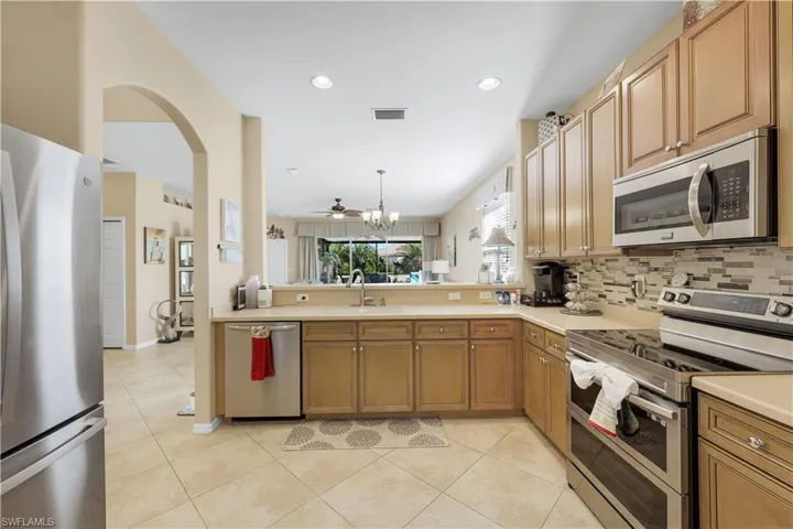 Kitchen with stainless steel appliances, light countertops, arched walkways, light tile patterned flooring, and recessed lighting