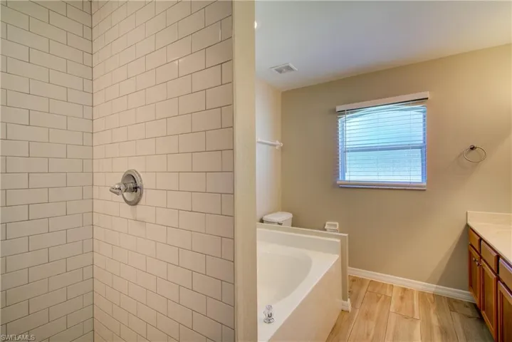 Bathroom featuring vanity, a garden tub, wood finish floors, and a tile shower