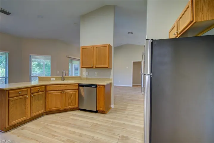 Kitchen featuring stainless steel appliances, vaulted ceiling, light wood-type flooring, a peninsula, and brown cabinets