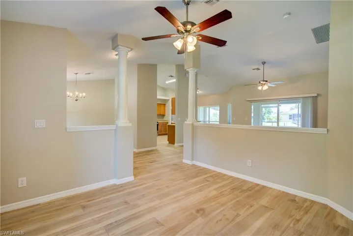 Spare room featuring light wood-style floors, a ceiling fan, a chandelier, vaulted ceiling, and ornate columns