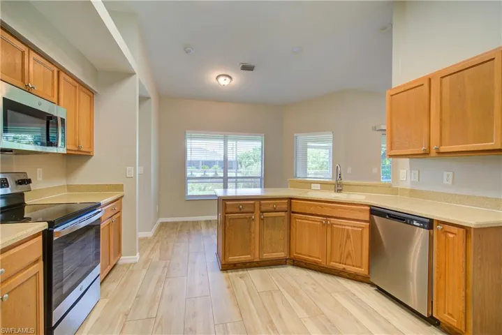 Kitchen with appliances with stainless steel finishes, a peninsula, light wood-type flooring, brown cabinetry, and light stone counters