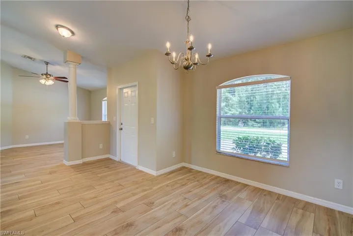 Empty room featuring light wood-style flooring, decorative columns, ceiling fan, and a chandelier