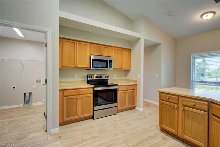 Kitchen featuring appliances with stainless steel finishes, lofted ceiling, brown cabinetry, wood finish floors, and light stone countertops