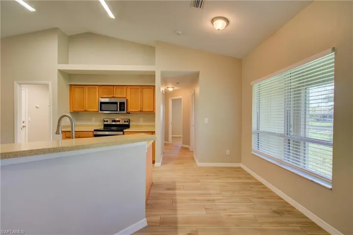 Kitchen featuring appliances with stainless steel finishes, light wood-style floors, lofted ceiling, and light stone counters