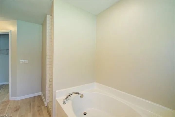 Bathroom with a spacious closet, a bath, and wood finished floors