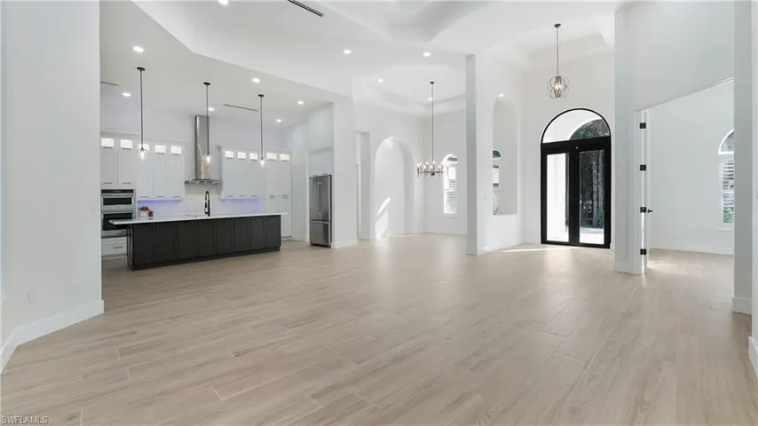 Unfurnished living room with a chandelier, a high ceiling, light wood finished floors, arched walkways, and recessed lighting