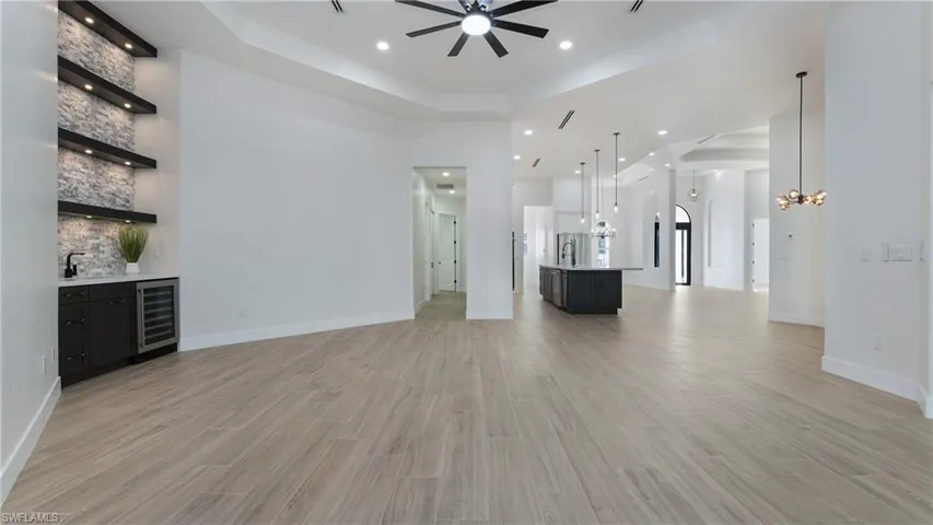 Unfurnished living room with a tray ceiling, light wood-type flooring, wine cooler, recessed lighting, and bar with sink