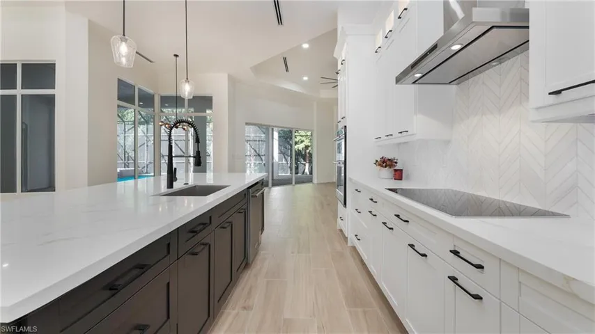 Kitchen with white cabinets, light stone counters, decorative light fixtures, wall chimney range hood, and backsplash