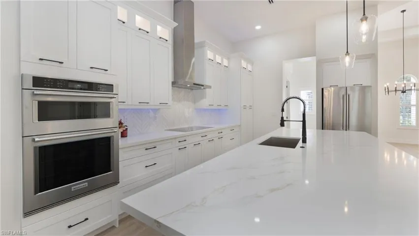 Kitchen featuring stainless steel appliances, hanging light fixtures, light stone counters, wall chimney exhaust hood, and recessed lighting