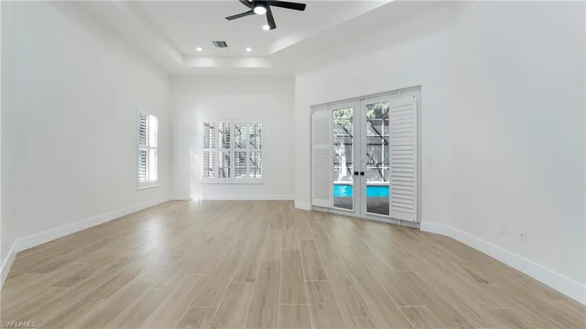 Empty room with french doors, wood tiled floors, ceiling fan, a tray ceiling, and a towering ceiling