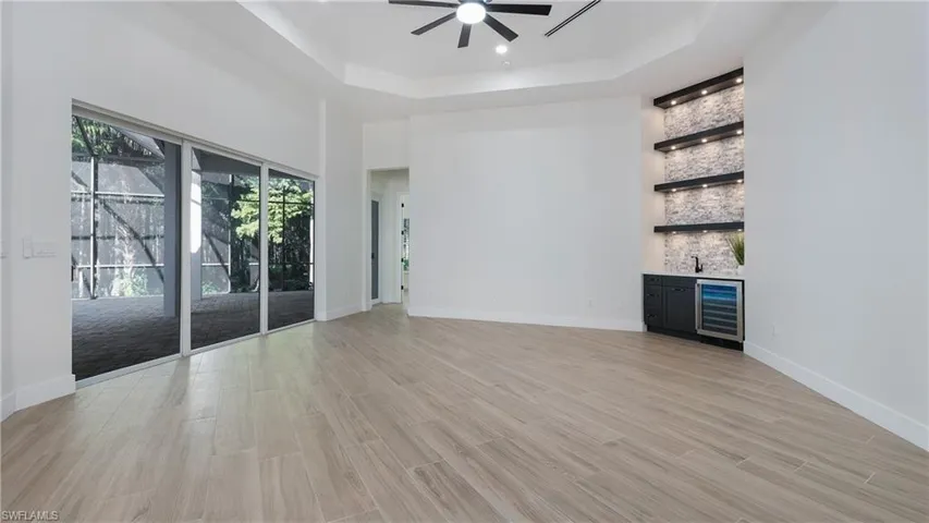 Unfurnished living room with beverage cooler, a ceiling fan, light wood-style floors, a tray ceiling, and a towering ceiling
