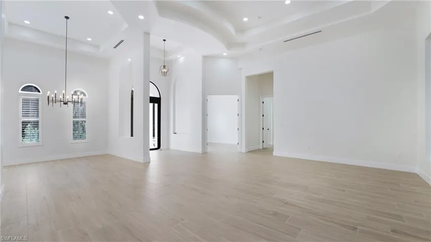 Unfurnished living room featuring a raised ceiling, a towering ceiling, a chandelier, light wood-style floors, and recessed lighting