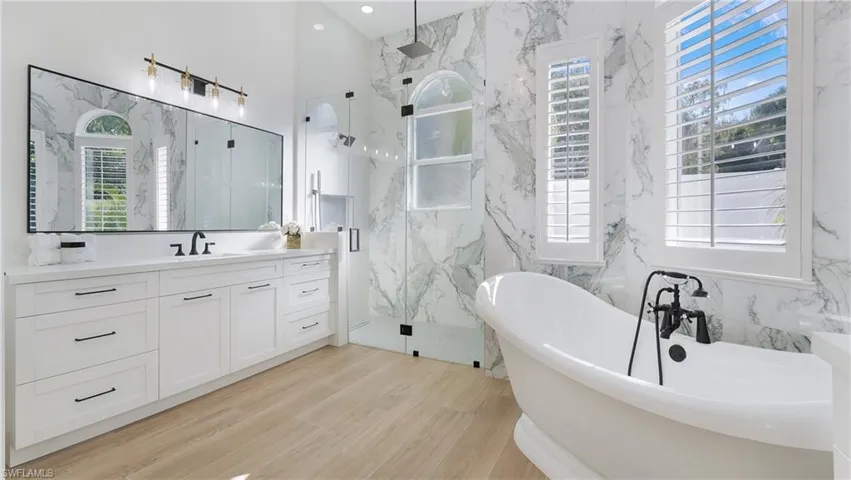 Bathroom featuring a freestanding bath, healthy amount of natural light, a marble finish shower, vanity, and tile walls