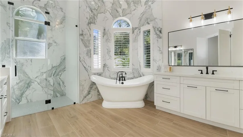 Full bathroom with vanity, a marble finish shower, a freestanding bath, tile walls, and wood tiled floors