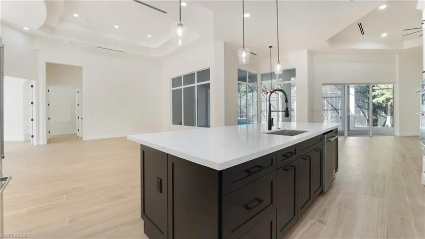 Kitchen featuring a raised ceiling, open floor plan, hanging light fixtures, wood finish floors, and recessed lighting