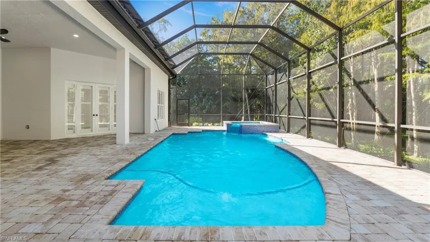 View of swimming pool featuring a lanai, a patio, a pool with connected hot tub, a sunroom, and french doors