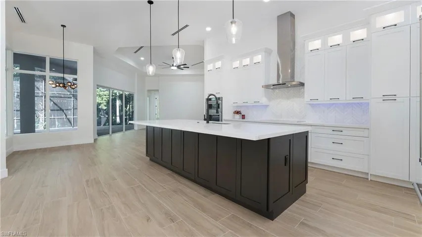 Kitchen with decorative backsplash, glass insert cabinets, white cabinetry, hanging light fixtures, and recessed lighting