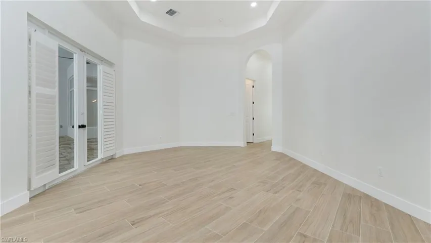 Unfurnished room featuring a tray ceiling, wood tiled floors, arched walkways, a towering ceiling, and recessed lighting