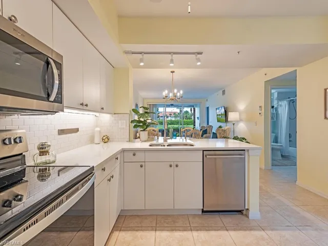 Kitchen featuring a notable chandelier, stainless steel appliances, sink, white cabinets, and kitchen peninsula