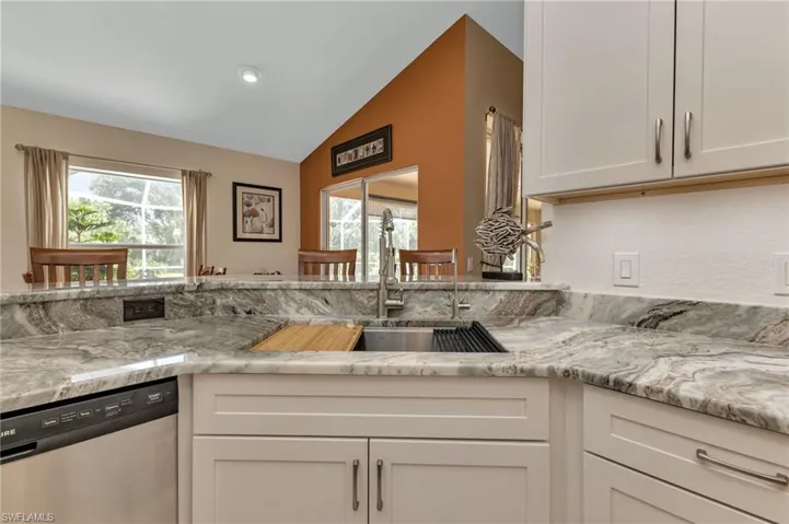 Kitchen featuring white cabinetry, dishwasher, vaulted ceiling, and light stone countertops