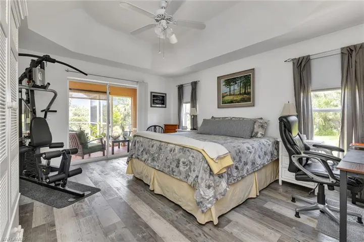 Bedroom featuring ceiling fan, access to outside, light hardwood / wood-style flooring, and a raised ceiling