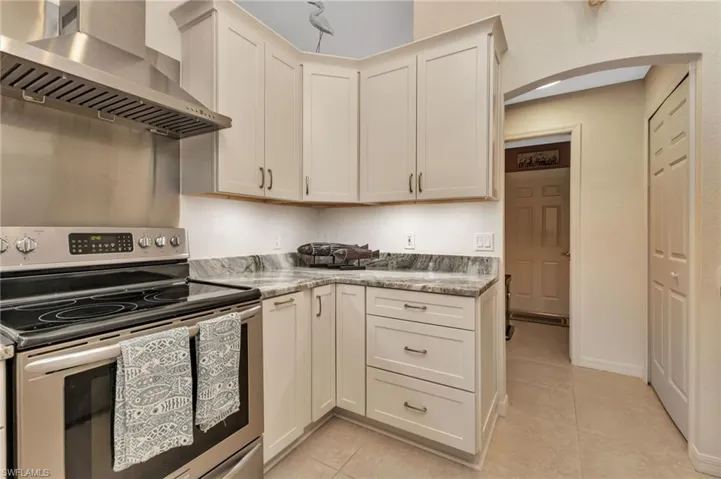 Kitchen featuring light stone counters, light tile patterned floors, wall chimney exhaust hood, and stainless steel electric stove