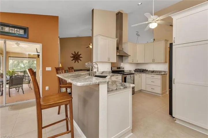 Kitchen featuring electric range, wall chimney range hood, kitchen peninsula, and ceiling fan