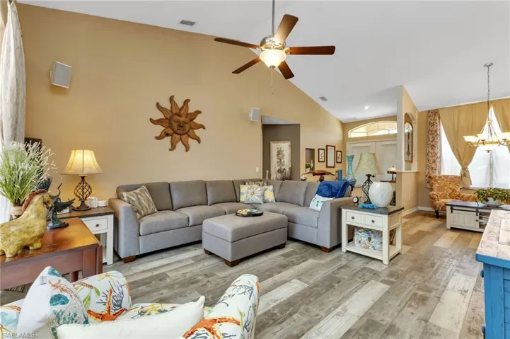 Living room with ceiling fan with notable chandelier, light hardwood / wood-style flooring, and high vaulted ceiling