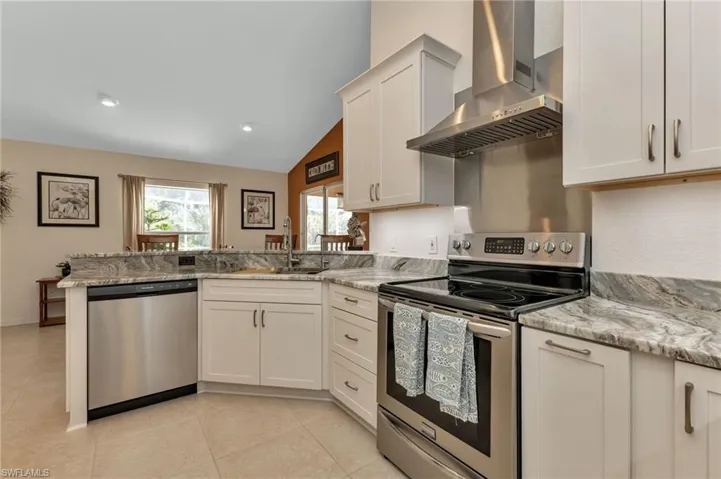 Kitchen with wall chimney range hood, white cabinets, sink, appliances with stainless steel finishes, and kitchen peninsula