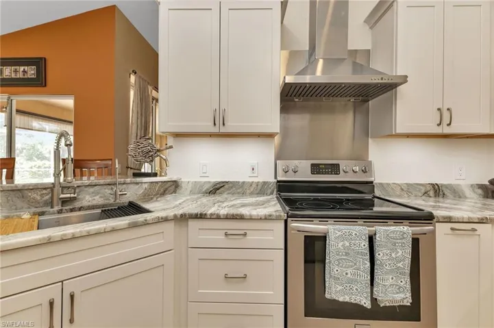 Kitchen with wall chimney exhaust hood, electric range, sink, light stone countertops, and lofted ceiling