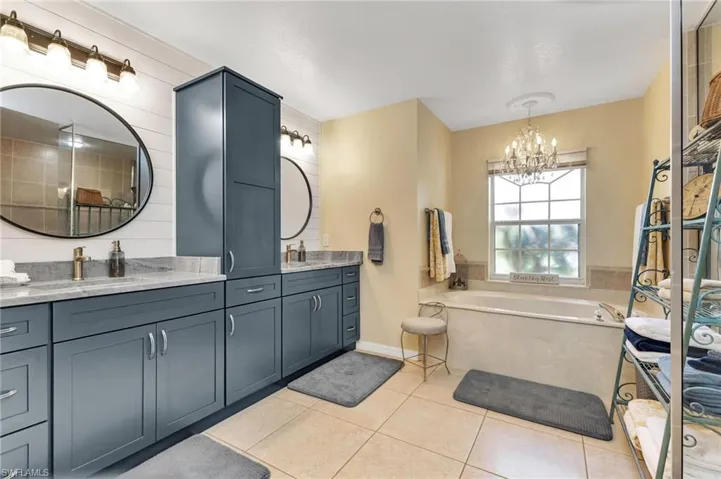 Bathroom with an inviting chandelier, tile patterned flooring, a bathtub, and double sink vanity