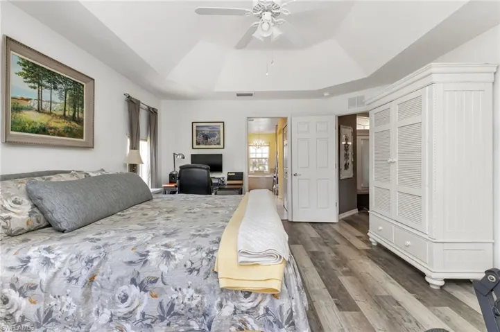 Bedroom featuring hardwood / wood-style flooring, multiple windows, ceiling fan, and a raised ceiling