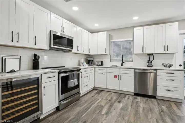 Kitchen with wood-type flooring, stainless steel appliances, decorative backsplash, sink, and wine cooler